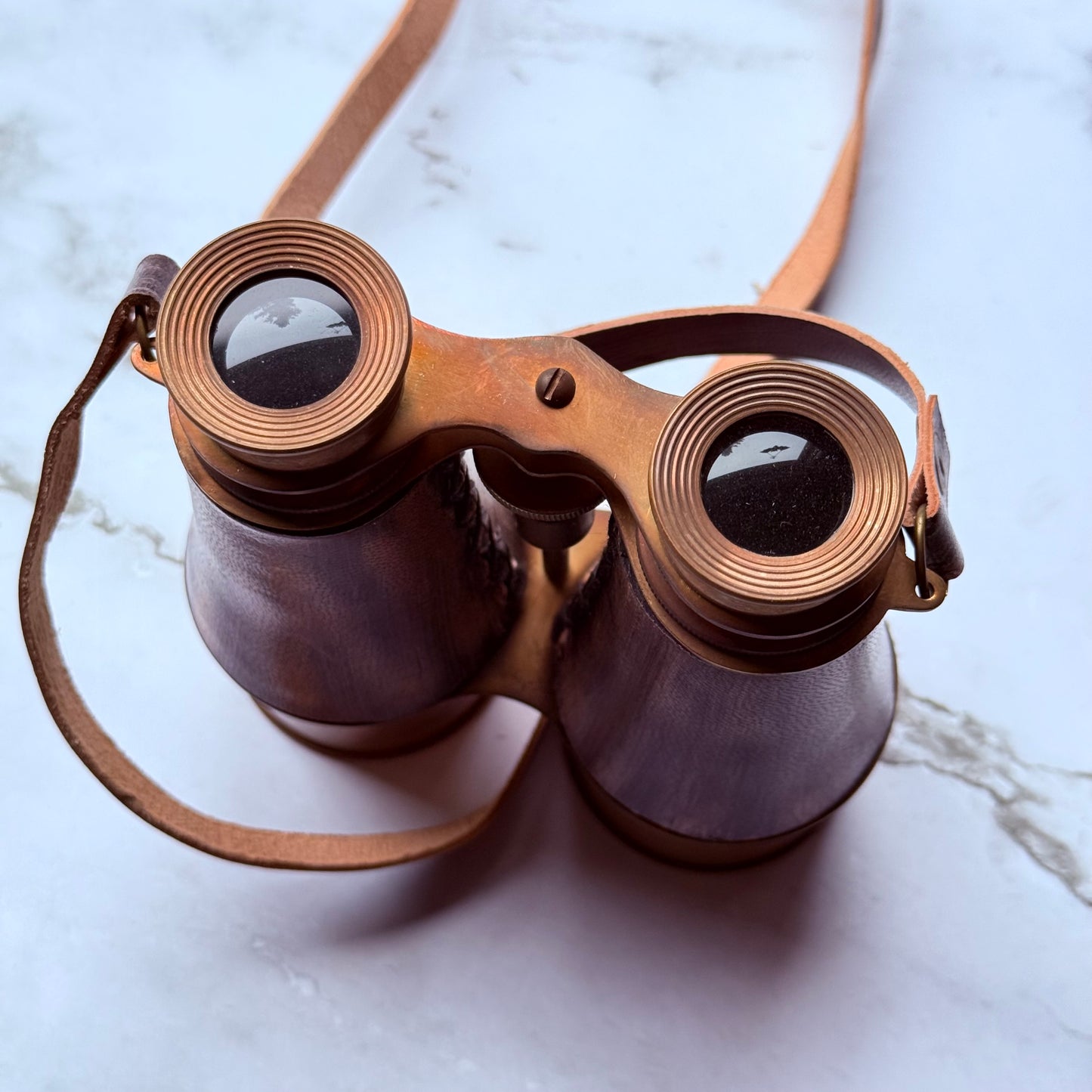 Vintage-style binoculars with a leather strap on a marble surface
