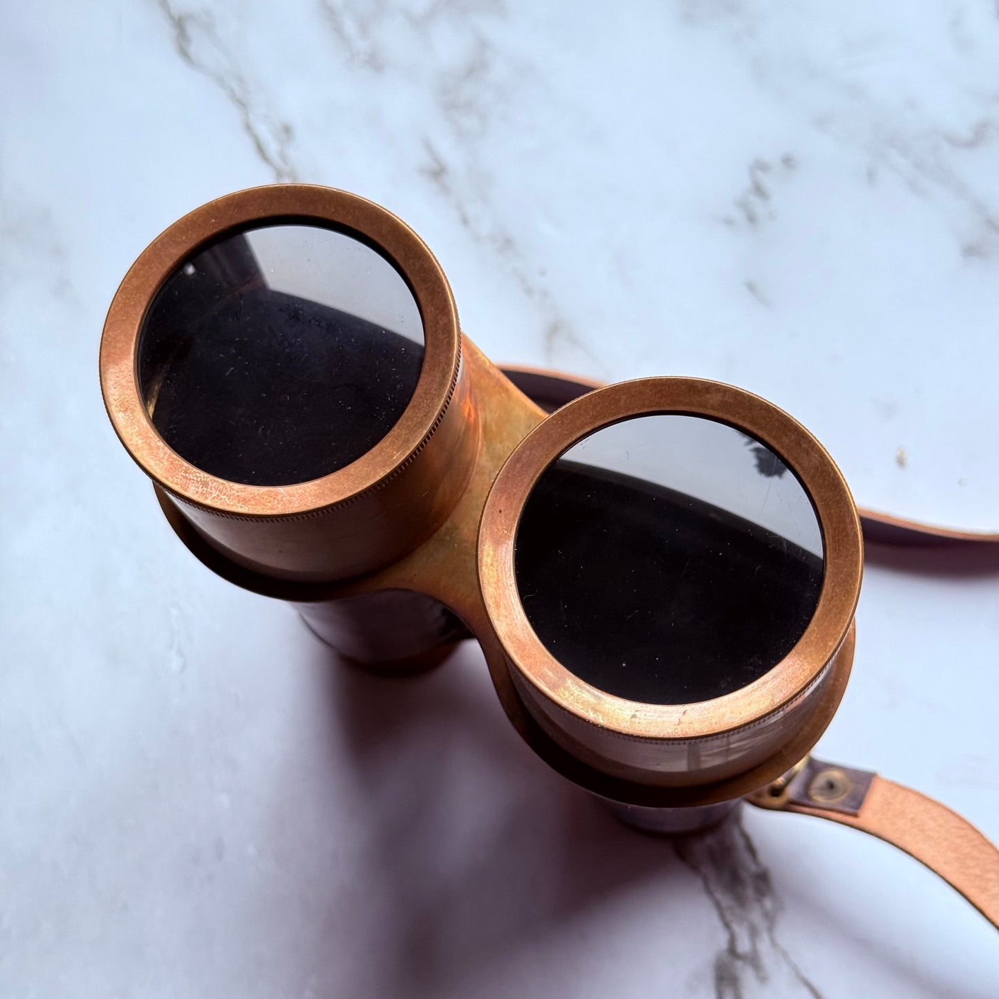 Vintage-style binoculars with aged leather finish on a marble surface