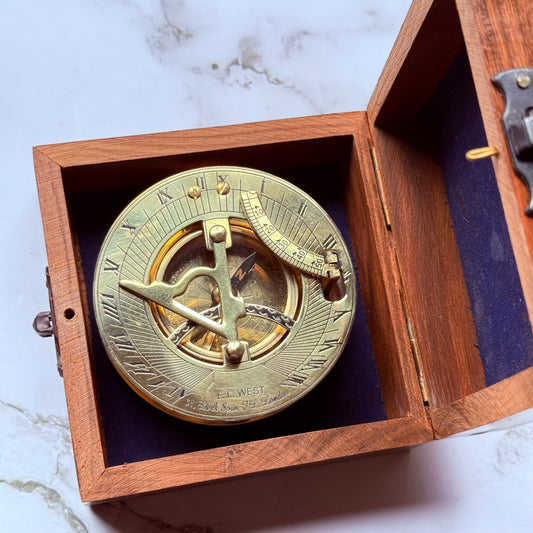 Brass sundial compass in a wooden box on a marble surface