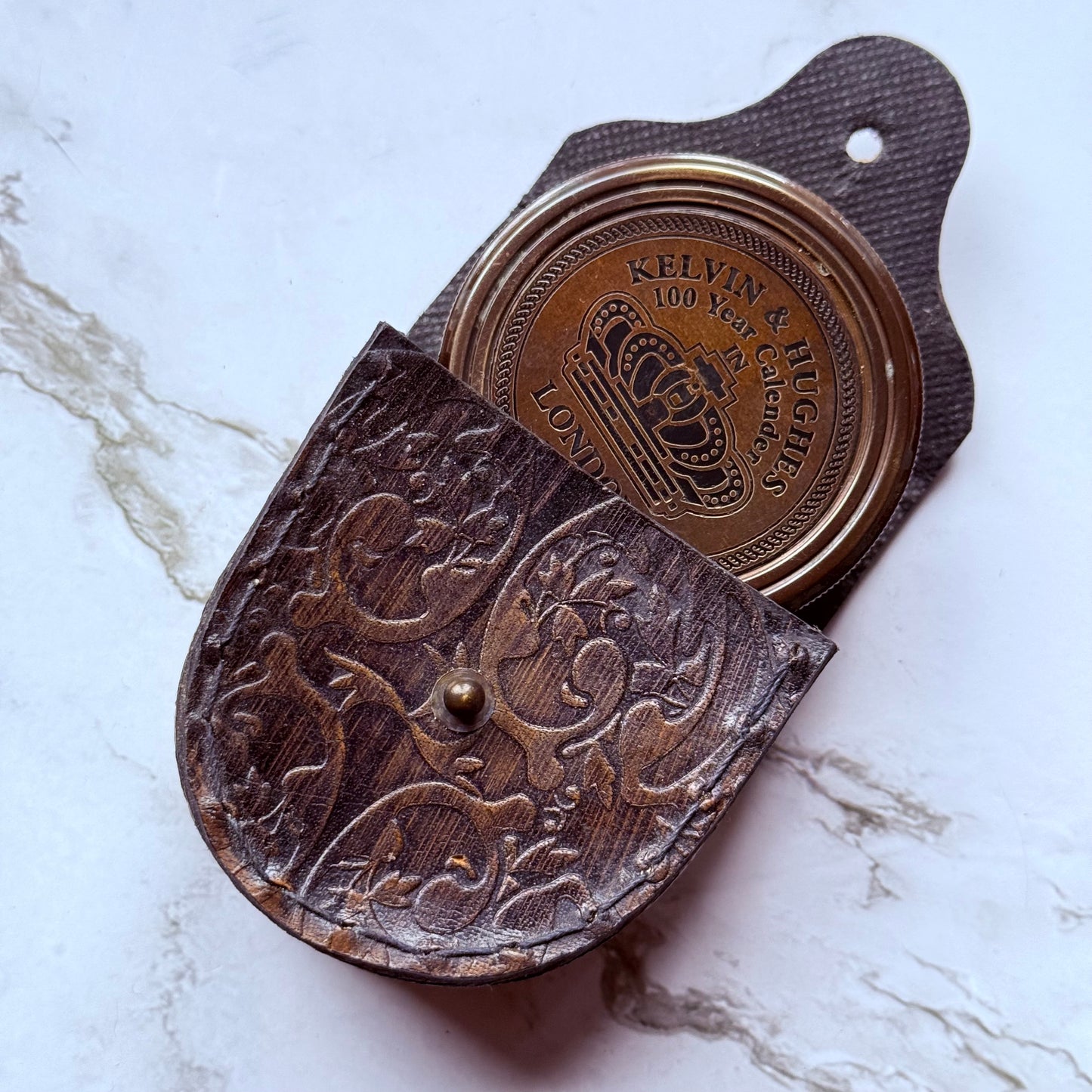 A closed bronze compass tucked partly into leather pouch embossed in a floral design