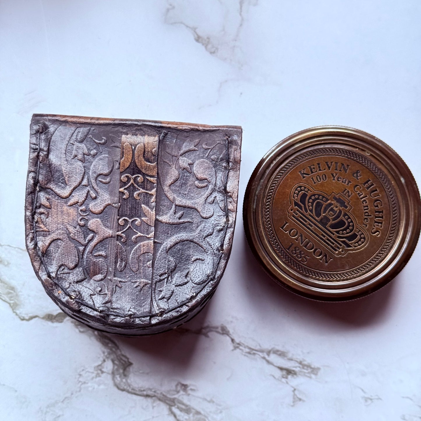 A closed bronze compass and leather pouch embossed in a floral design