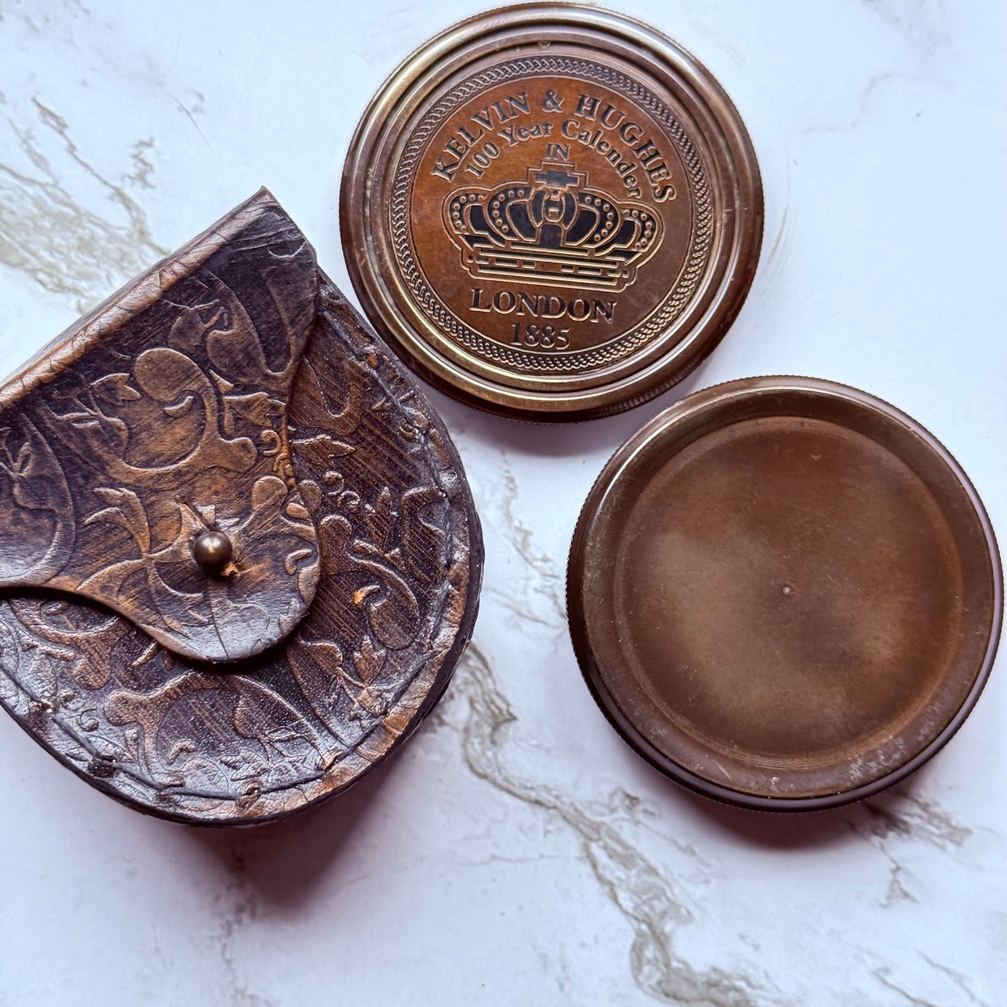 Lid next to a bronze compass and leather pouch embossed in a floral design