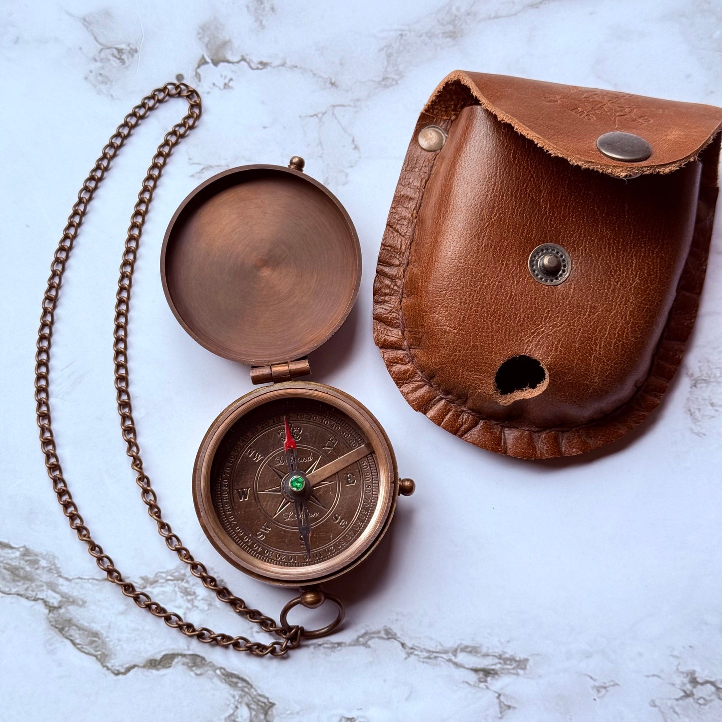 Bronze pocket compass with chain and leather case on a marble surface