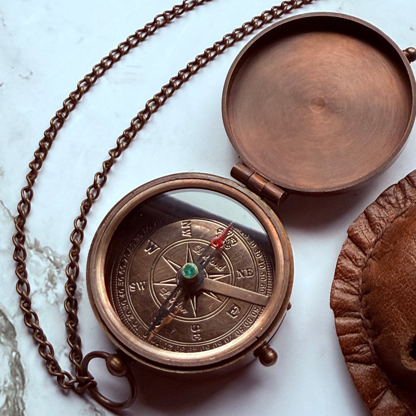 Bronze compass with chain on a marble surface