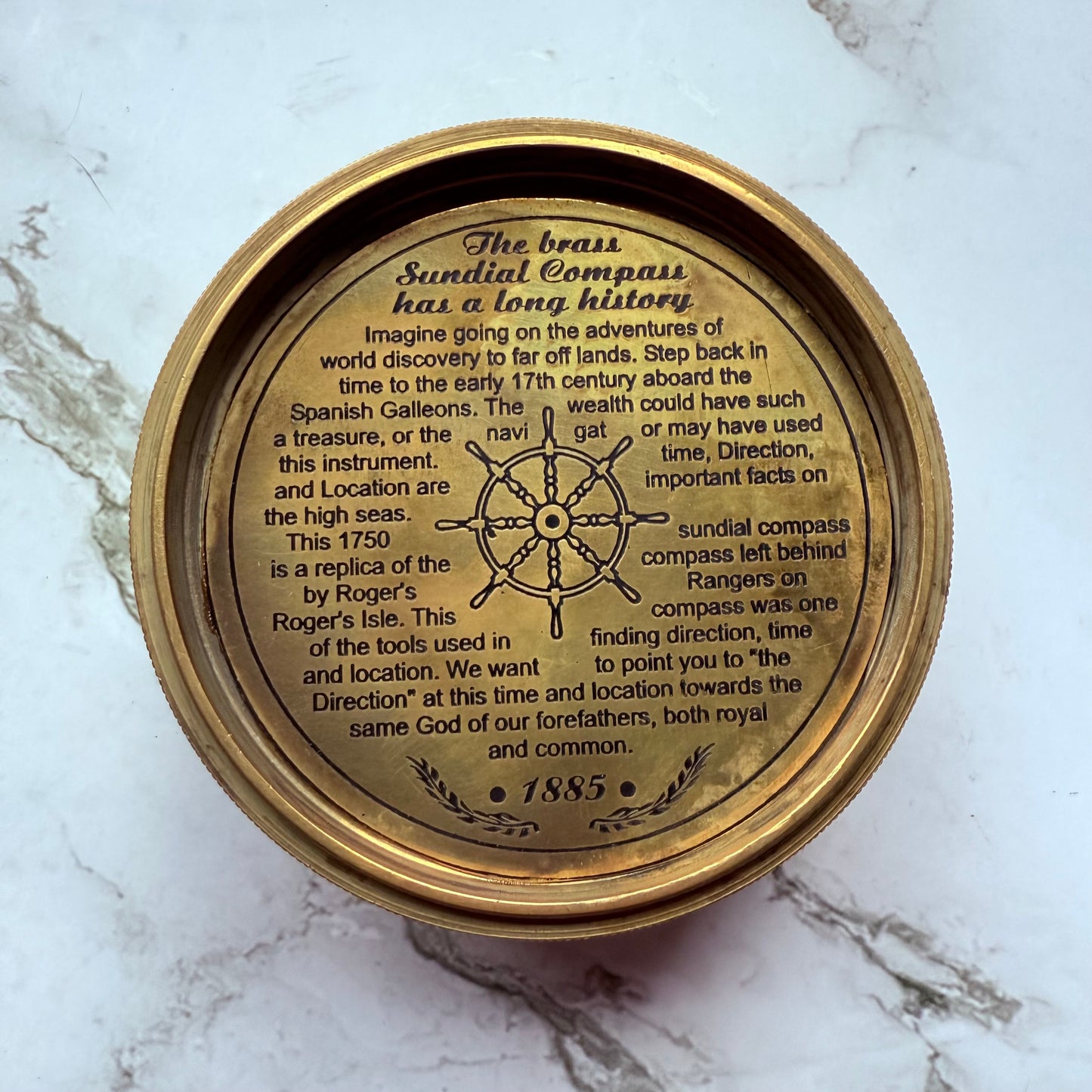 Brass sundial compass with engraved text on a marble surface