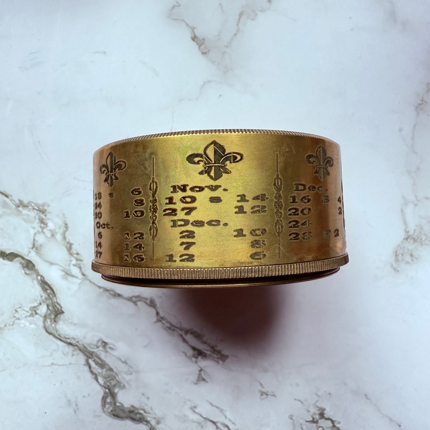 Brass container with engraved numbers and dates on a marble surface