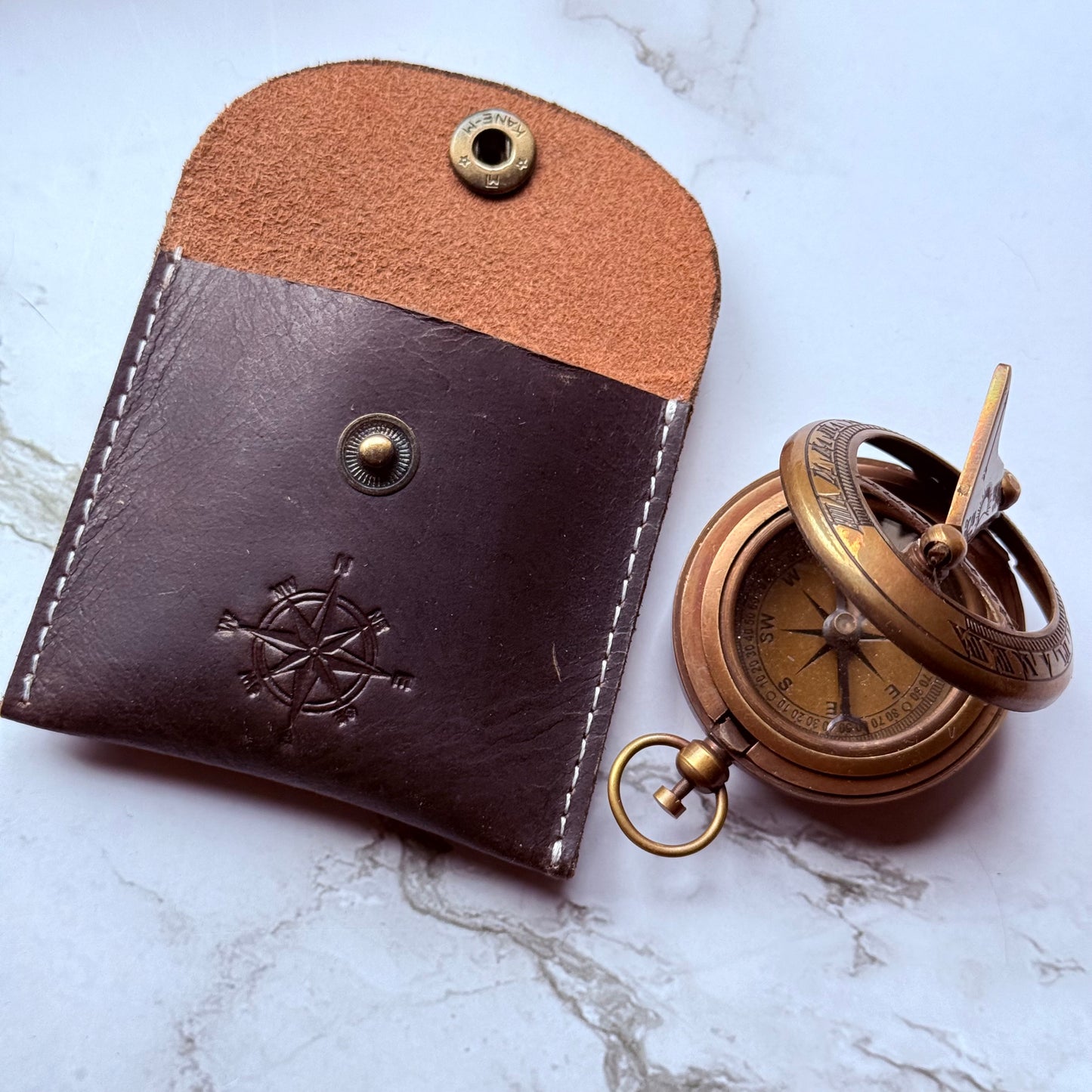Brown leather case with a pocket sundial compass on a white marble surface