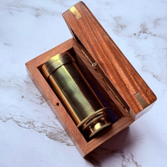 Brass collapsed mini spyglass in a wooden box on a marble surface
