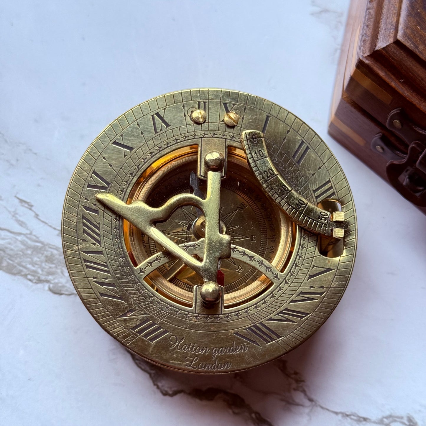Brass sundial compass on a marble surface with a wooden box in the background