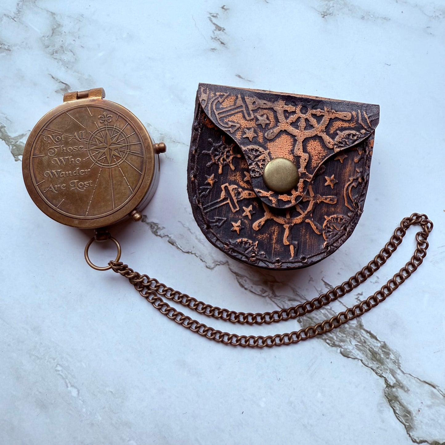Bronze compass and leather case with chain on a marble surface