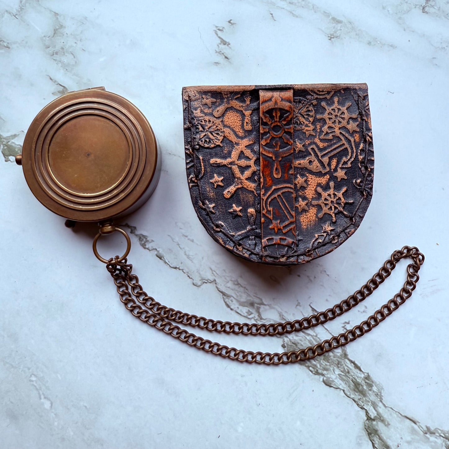 Bronze compass and decorative leather case on a marble surface
