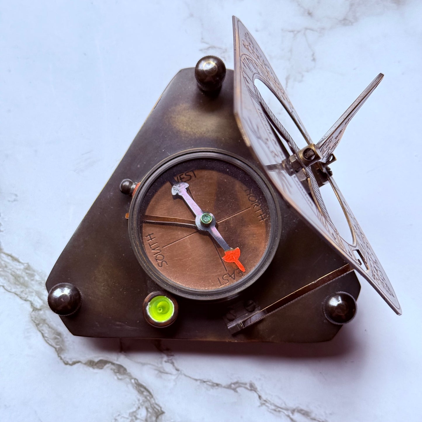 Triangular brass compass sundial on a marble surface