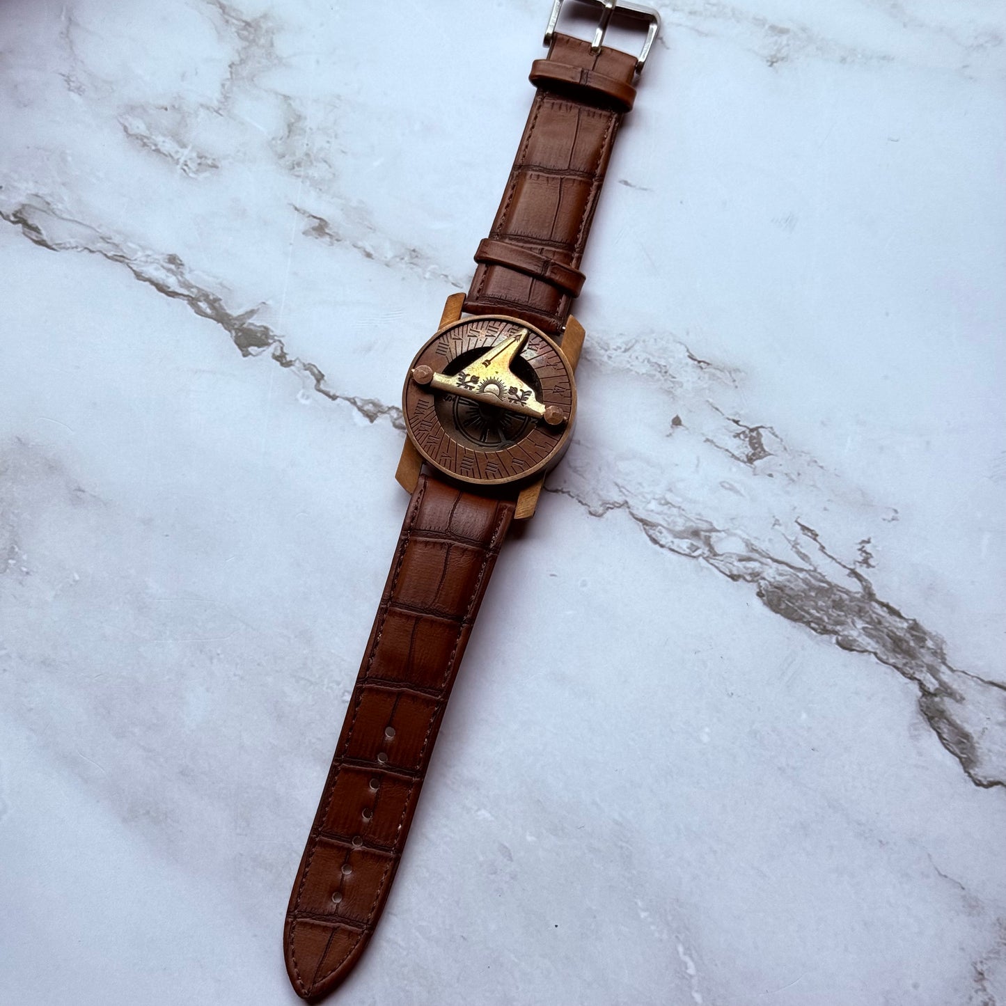 Sundial compass with brown leather strap on a marble surface