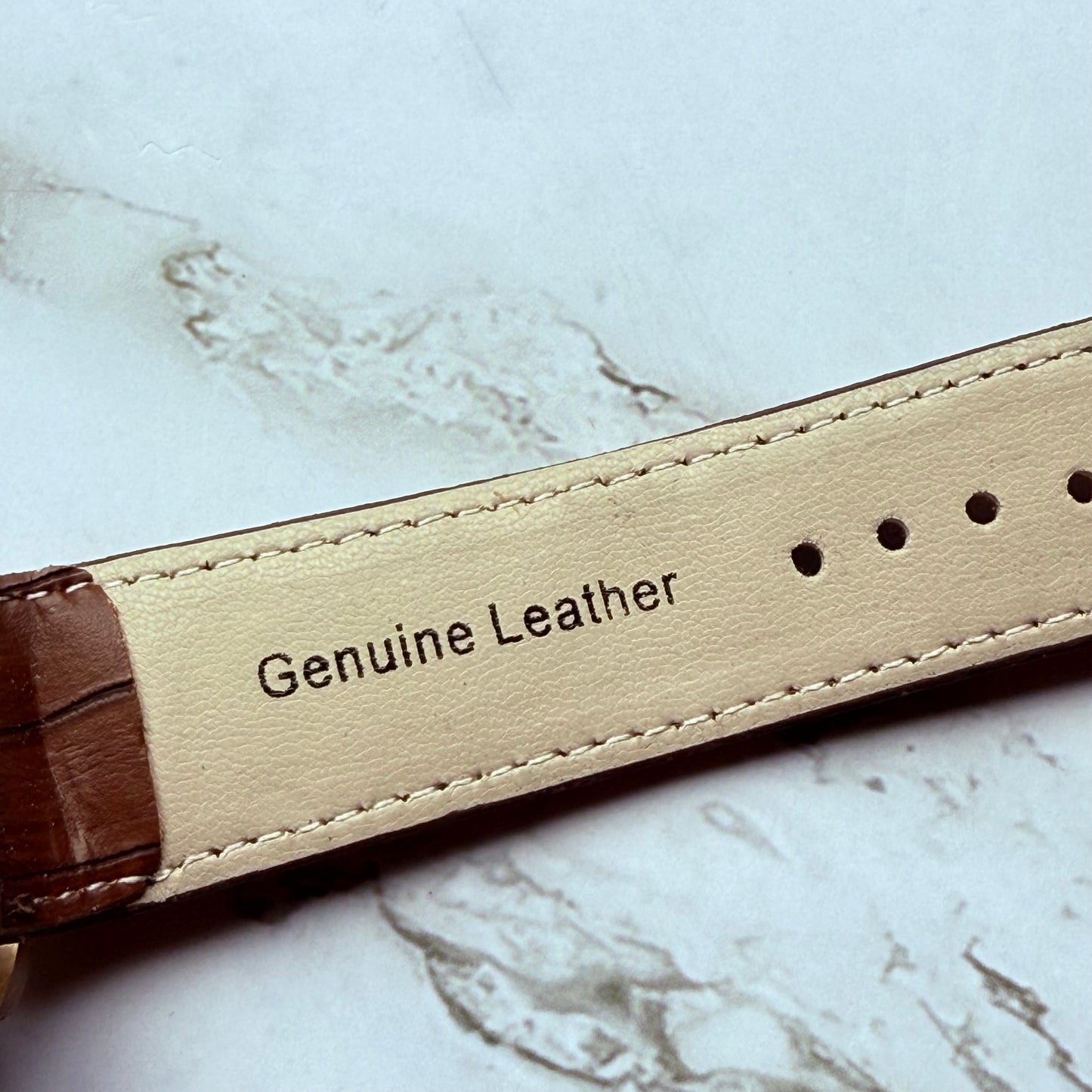 Close-up of a leather strap with 'Genuine Leather' label on a marble surface