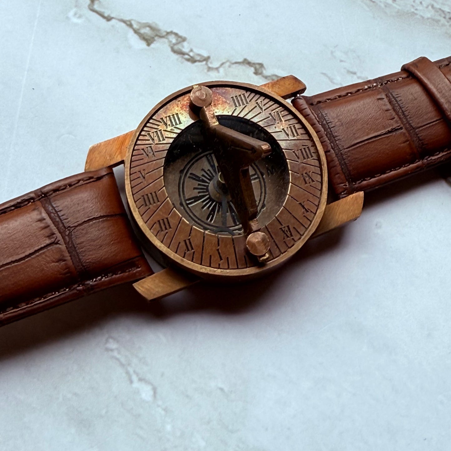 Bronze compass sundial with a detailed face on a marble surface