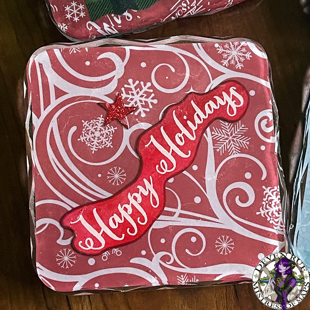 A close up of a coaster with red background, white swirls and snowflakes, and the words "Happy Holidays".