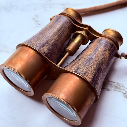 Vintage-style binoculars with aged leather finish on a marble surface