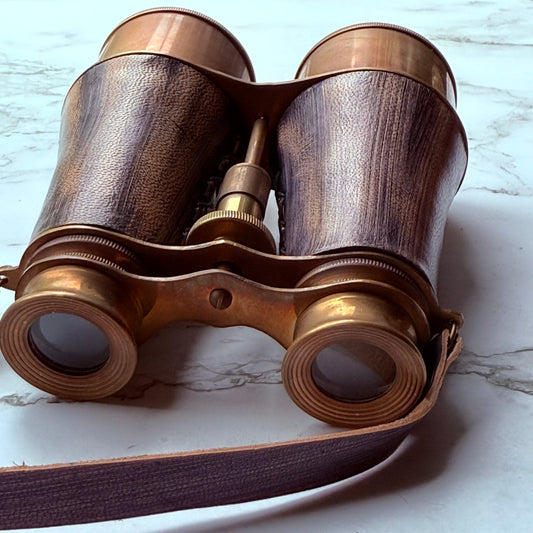 Vintage-style binoculars with aged leather finish on a marble surface