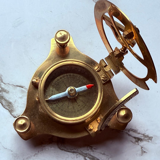 Open brass sundial compass on a marble surface