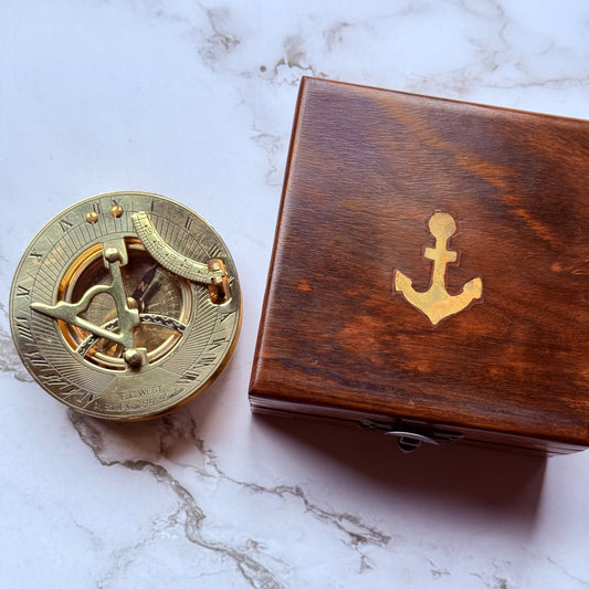 Brass compass and wooden box with anchor emblem on a marble surface