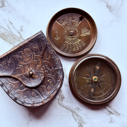 Underside of the lid next to a bronze compass and leather pouch embossed in a floral design