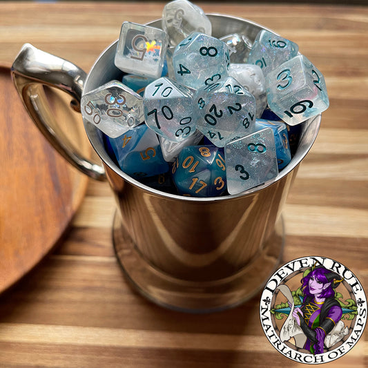 A three-quarter view of a shiny, silver tankard filled with blue dice topped with semi-transparent dice to mimic a tankard filled with a foamy beverage. The tankard is on a wood surface next to a wooden plate.