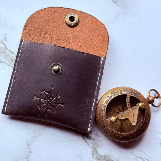 Brown leather case with a pocket sundial compass on a white marble surface