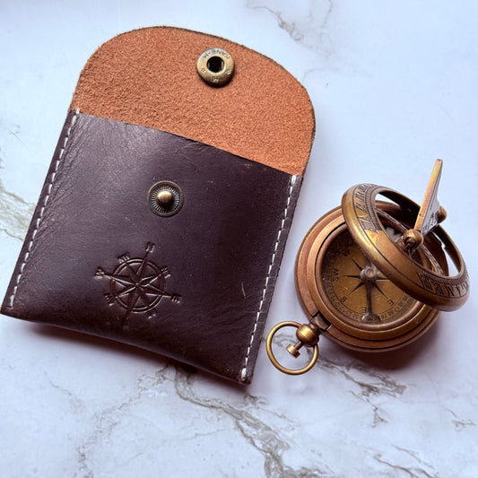 Brown leather case with a pocket sundial compass on a white marble surface