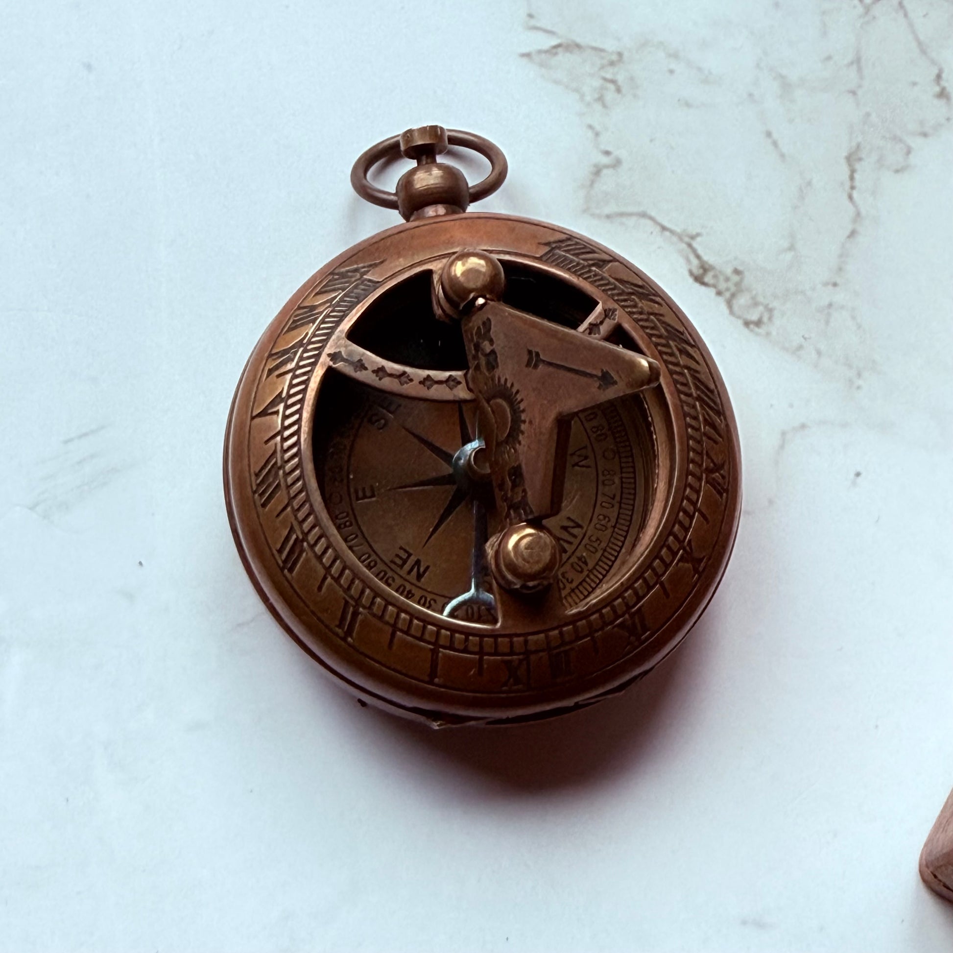 Bronze pocket sundial compass on a marble surface