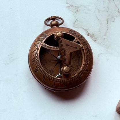 Bronze pocket sundial compass on a marble surface