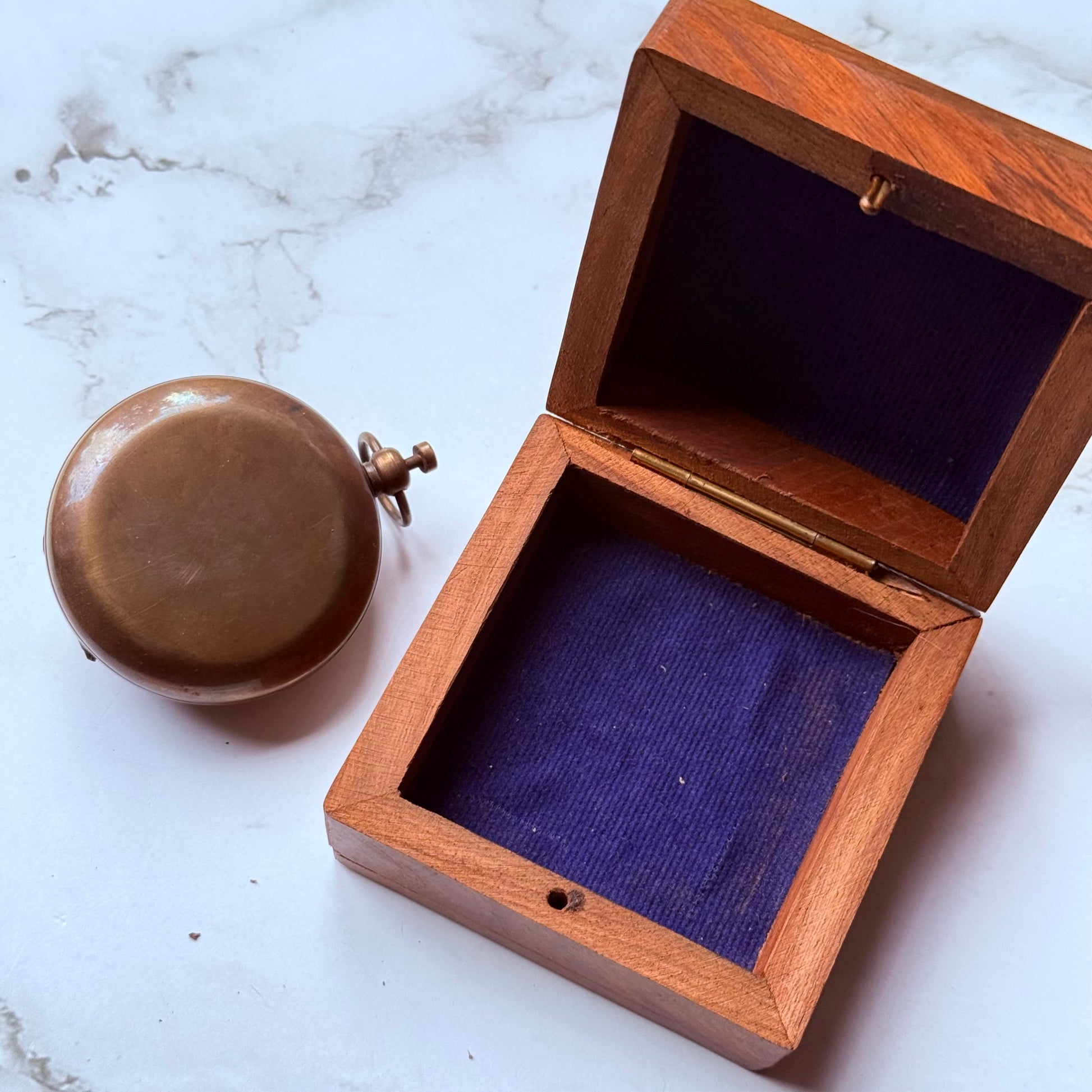 Wooden box with a blue interior next to a vintage pocket sundial compass on a marble surface