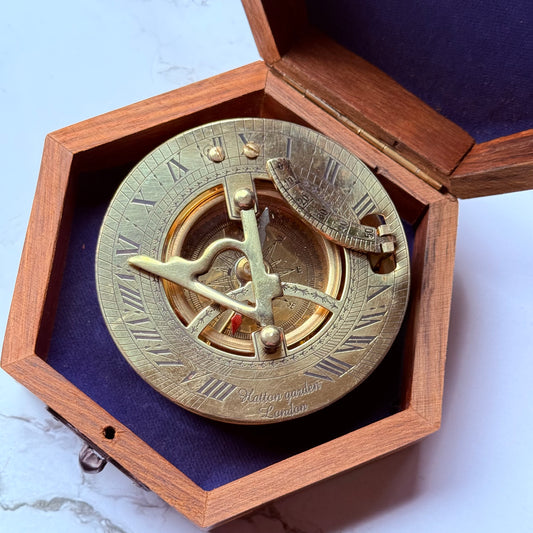 Brass sundial compass in a wooden box on a marble surface