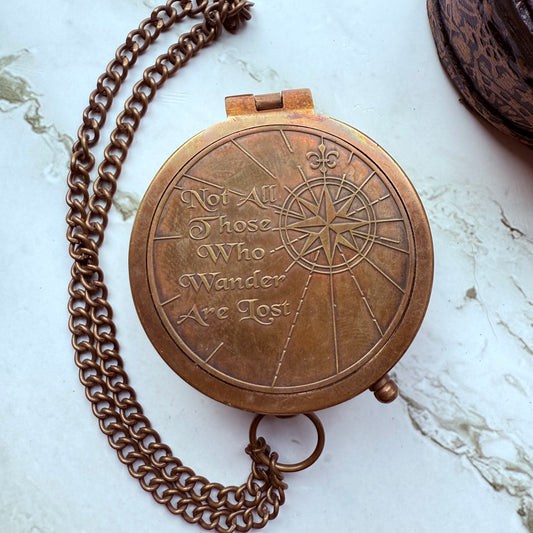 Bronze compass with 'Not All Those Who Wander Are Lost' quote on a marble surface