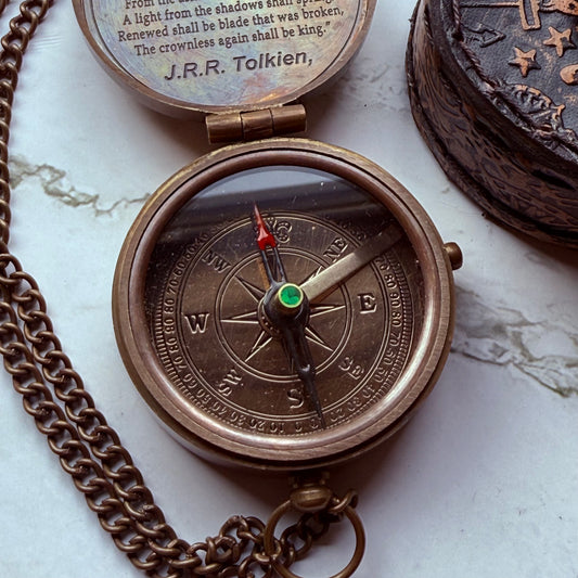 Bronze compass with chain on a marble surface, featuring text and symbols.