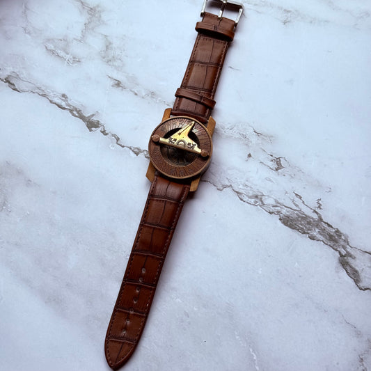 Sundial compass with brown leather strap on a marble surface
