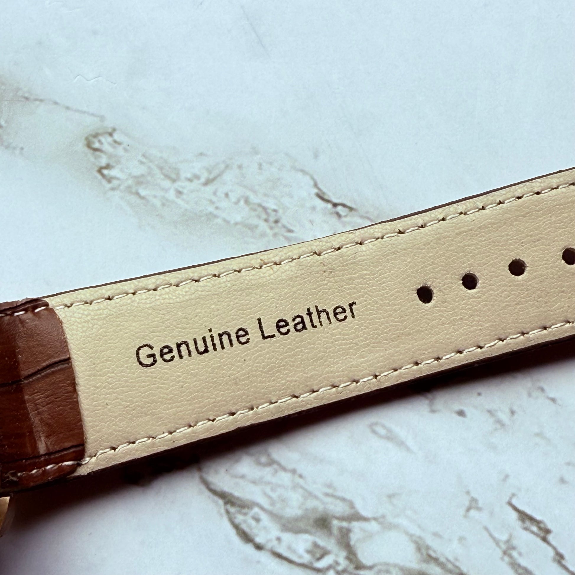 Close-up of a leather strap with 'Genuine Leather' label on a marble surface