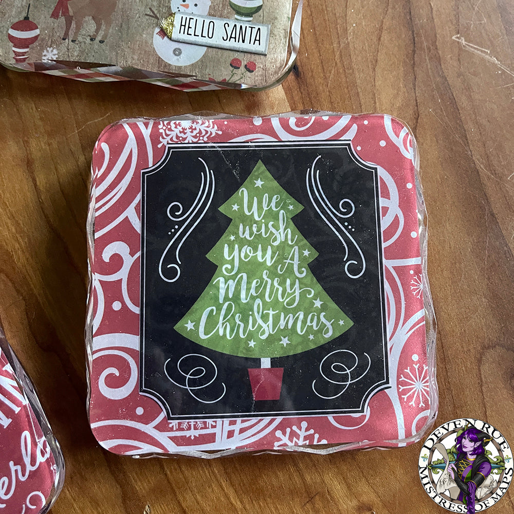 A close up of a resin coaster with art of a Christmas tree with the words "We wish you a merry Christmas" on it.