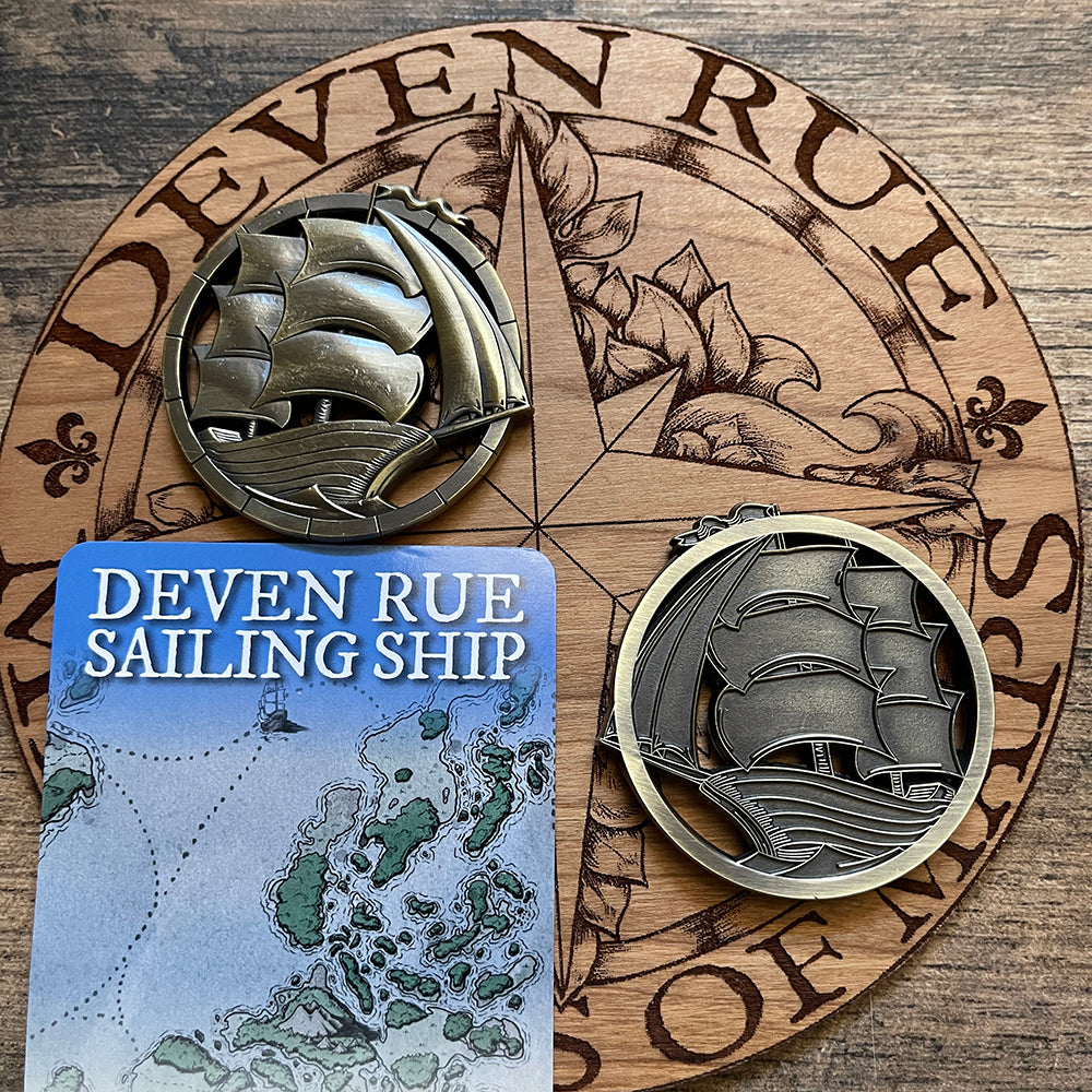 Two Ship Token map weights sit on the wooden Deven Rue logo to show front and back.