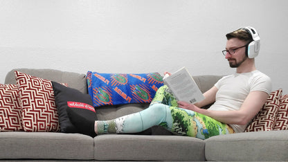 Josh Simons reads a book on a couch wearing the Queen's Treasure leggings by Deven Rue with a white tshirt.