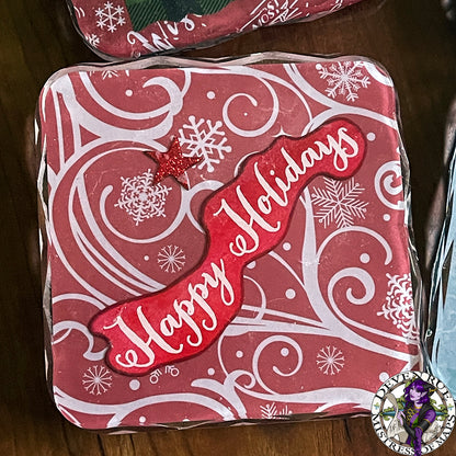 A close up of a coaster with red background, white swirls and snowflakes, and the words "Happy Holidays".