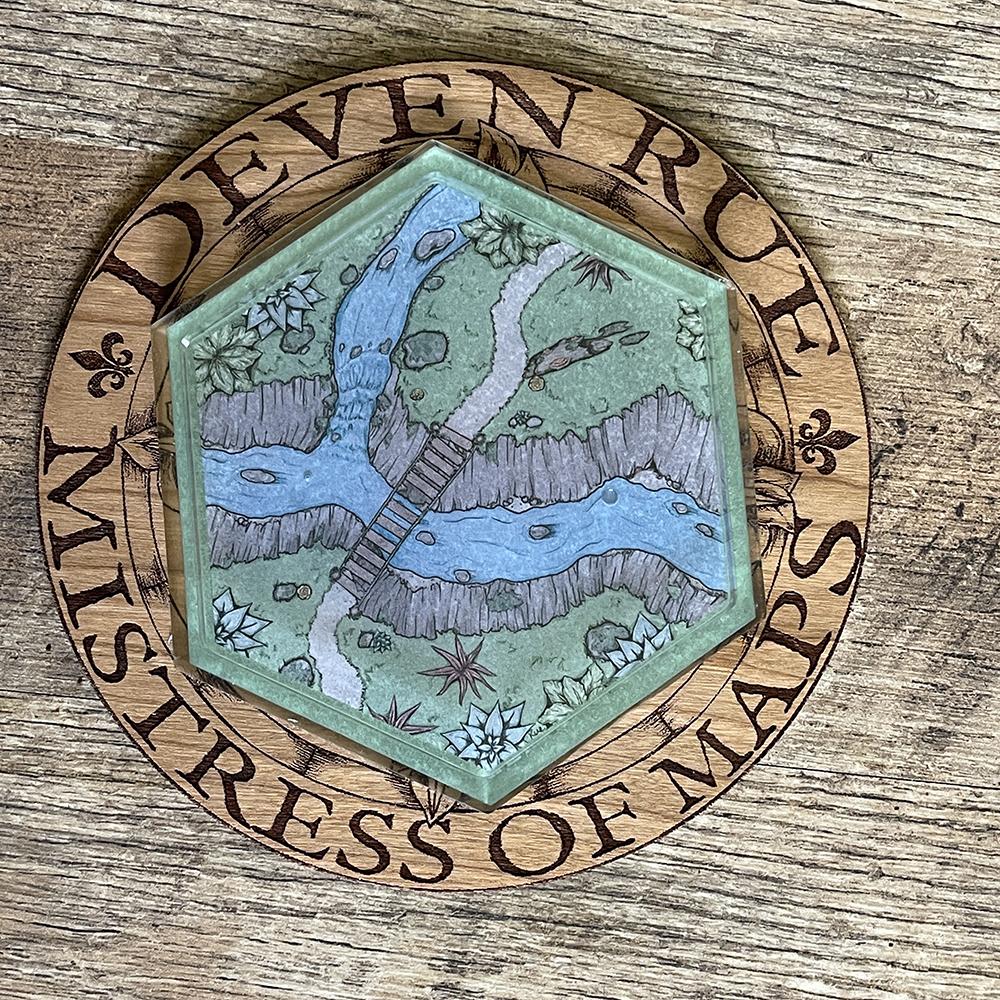 The Perilous Crossing Hex Map coaster on the wooden Deven Rue logo.