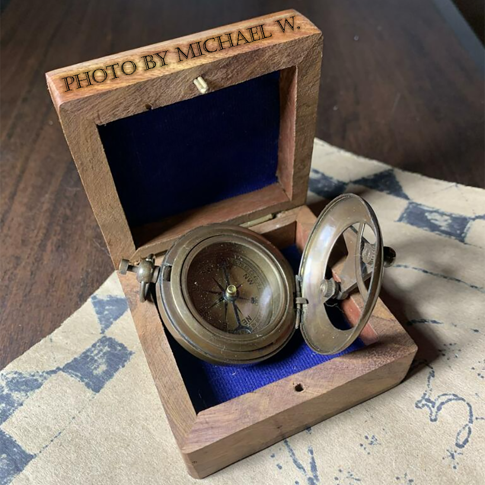 A photo of the compass and sundial open in their box on a faded parchment with "Photo by Michael W." seemingly wood burned into the top.