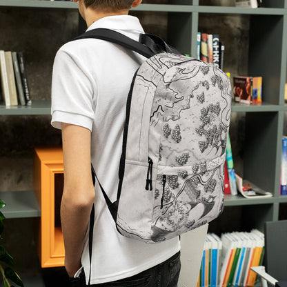 Side view: A model wears a backpack with the Humble Beginnings map by Deven Rue printed on it.