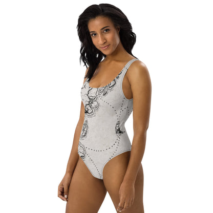 A model wears the Sailing into the Unknown one piece swimsuit by Deven Rue, left view.