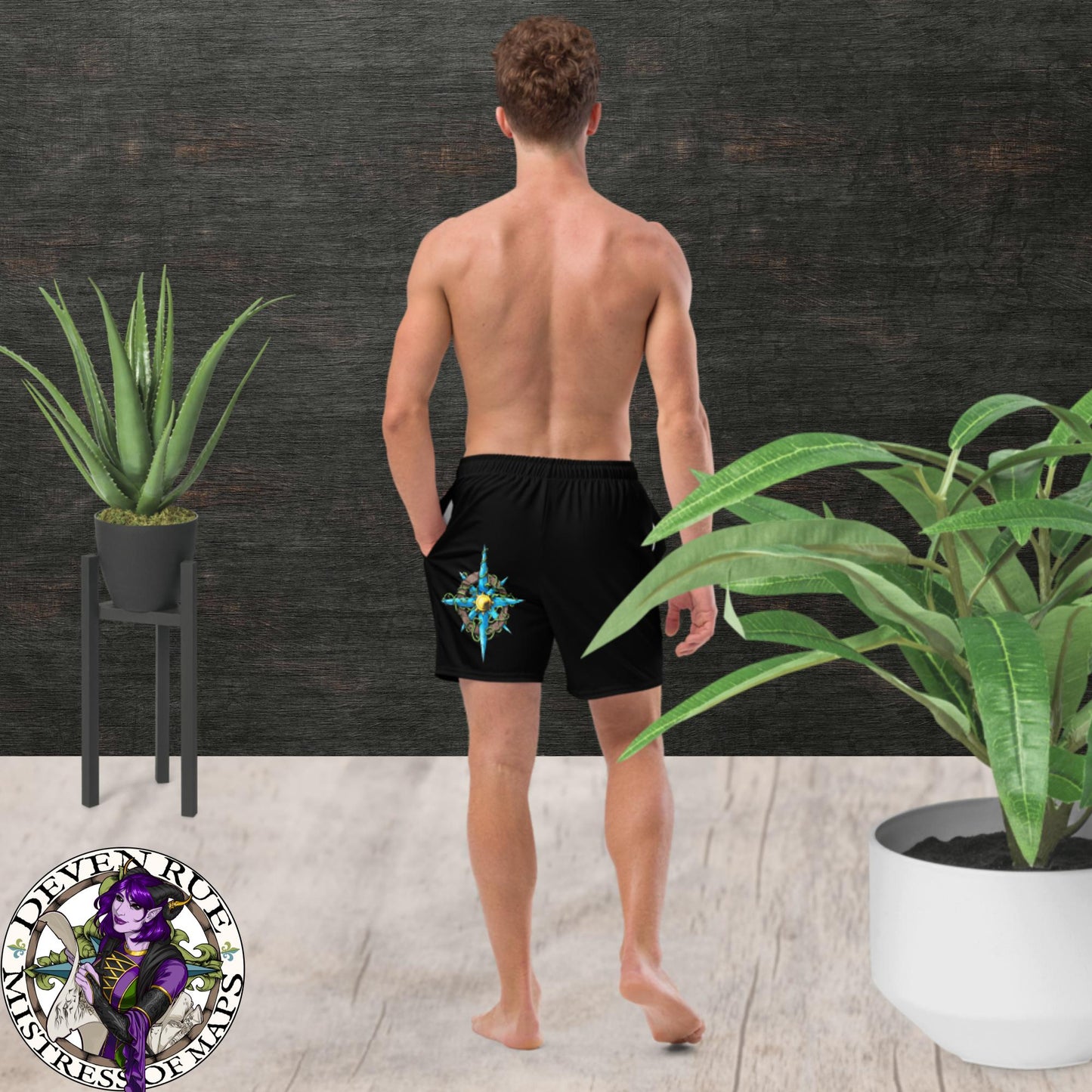 Back View: A model wears black swim trunks with the Wilds Compass Rose design on them.