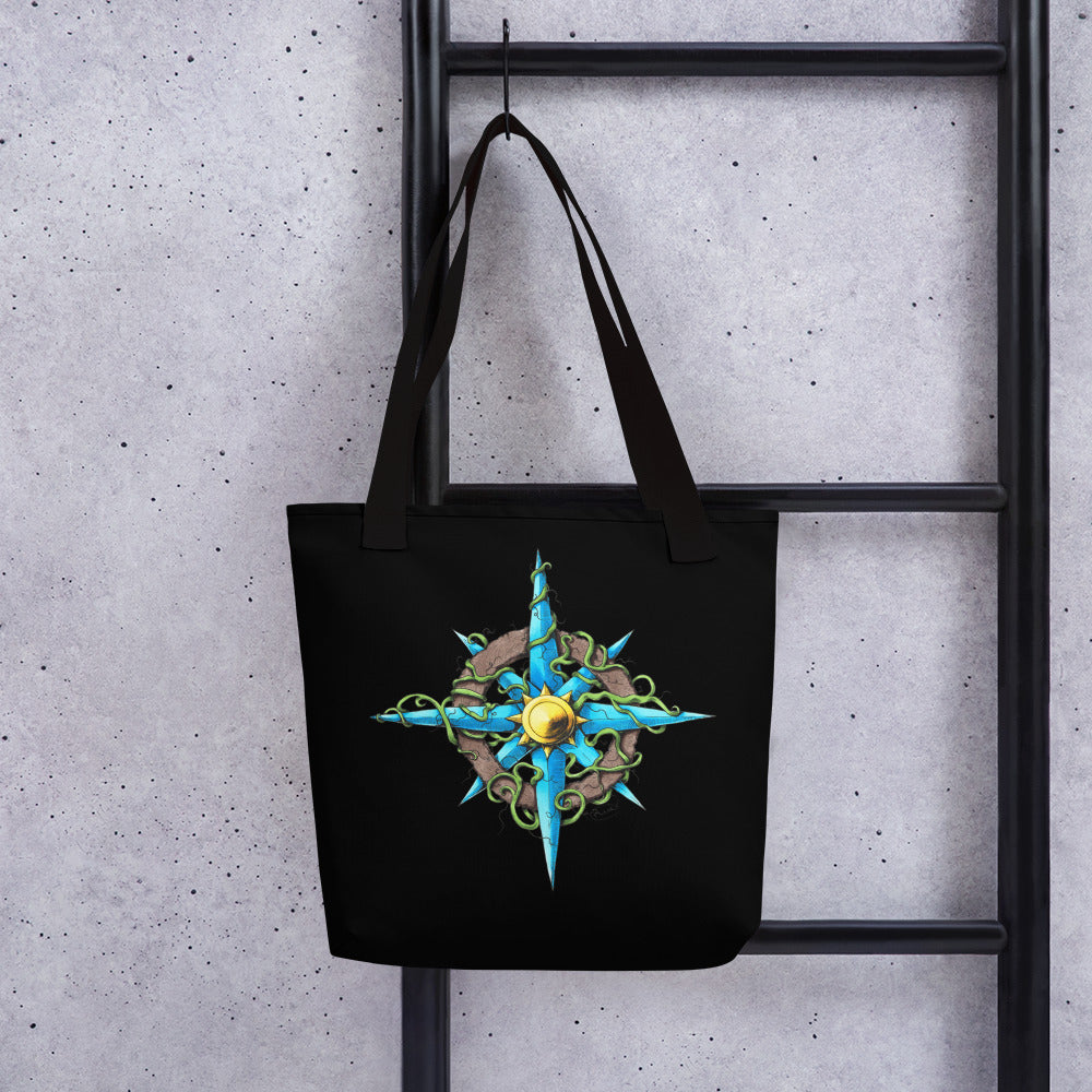 A tote bag with an illustration of a blue, brown, and gold compass taken over by vines hangs on a wall.