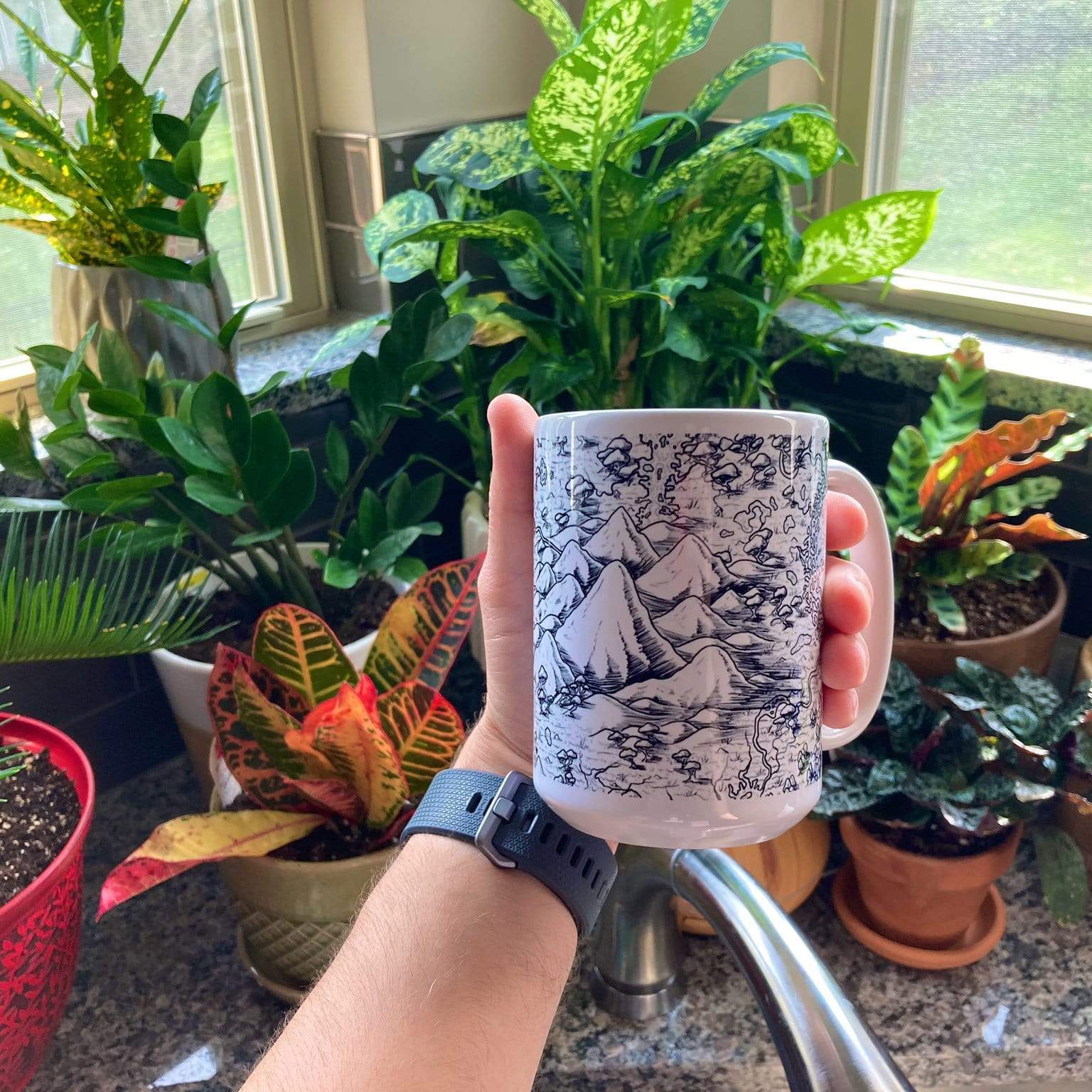 A hand holds the Forever Marshes map mug in front of many potted plants.