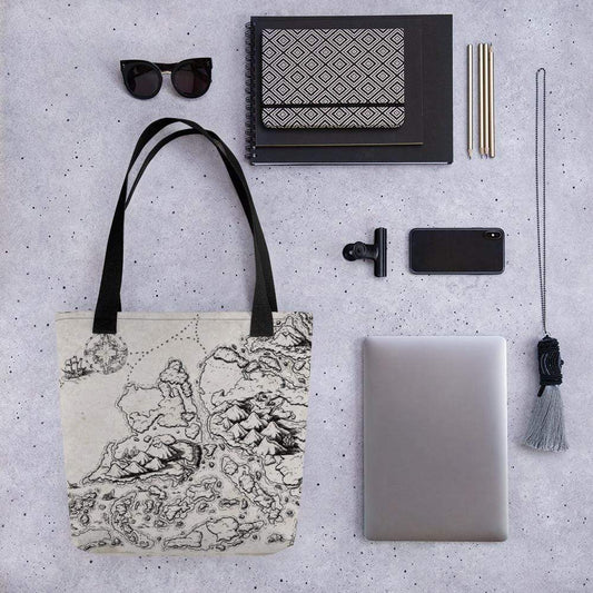 A tote bag with a black and white map illustration and black straps sits with sunglasses, books, phone, laptop, and other accessories for scale.