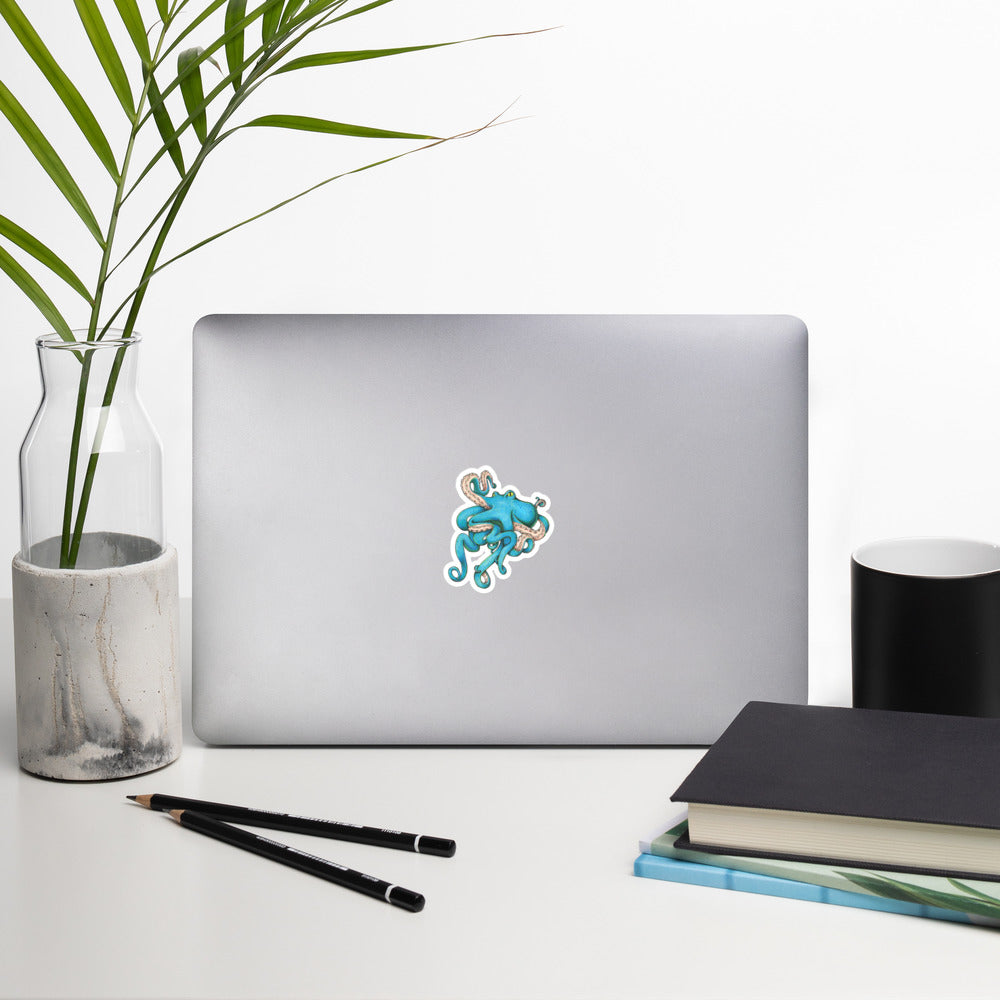 The 3" blue Tangled Octopus illustration sticker stuck to a laptop on a generic looking desk.
