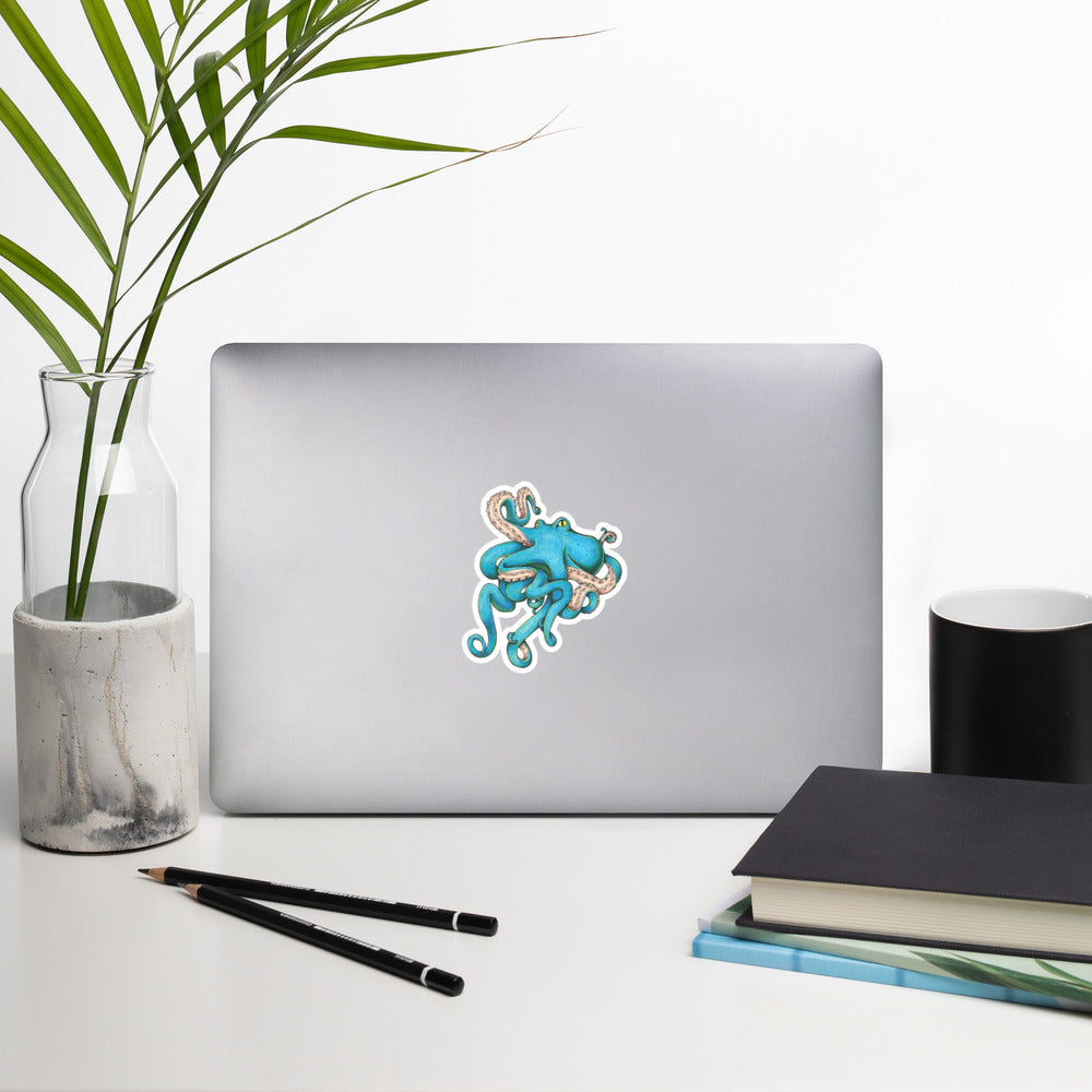 The 4" blue Tangled Octopus illustration sticker stuck to a laptop on a generic looking desk.